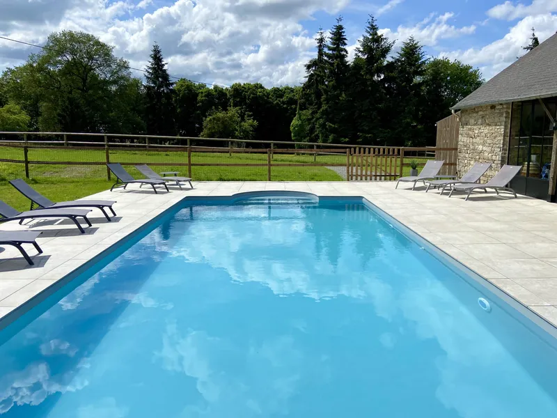 Piscine chauffée entourée de transats avec vue dégagée sur la prairie et les chevaux au pré