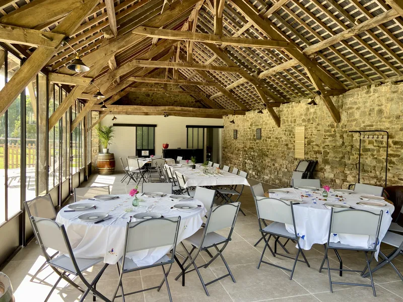 Grande salle de réception à charpente bois avec tables rondes dressées pour un repas de groupe