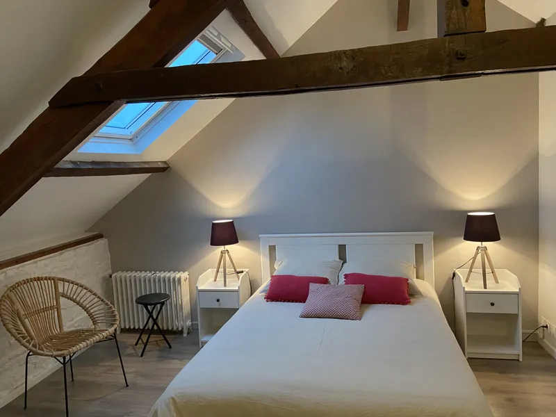 Chambre mansardée avec lit double, poutres apparentes, fenêtre de toit et lampes de chevet