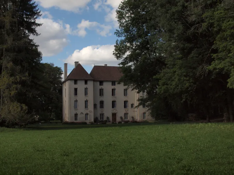 Façade sud du château vue depuis la prairie, toitures d'ardoise et tourelle entourées de grands arbres