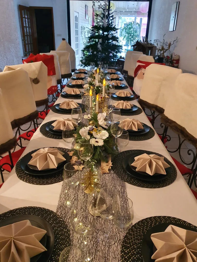 Grande salle à manger avec longue tablée dressée pour un repas de groupe et sapin décoré en arrière-plan
