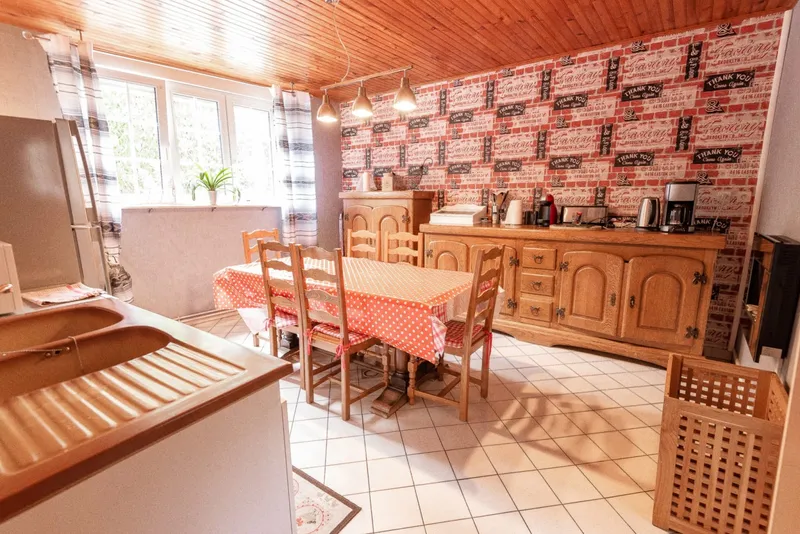 Cuisine équipée avec grande table à manger en bois habillée d'une nappe à carreaux et buffet ancien