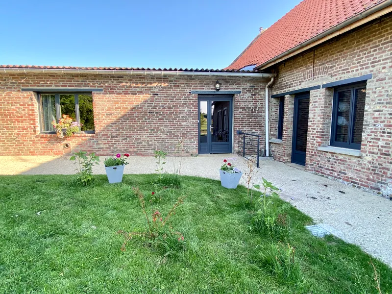 Façade en briques rouges de la ferme rénovée avec portes-fenêtres bleu marine et jardin fleuri