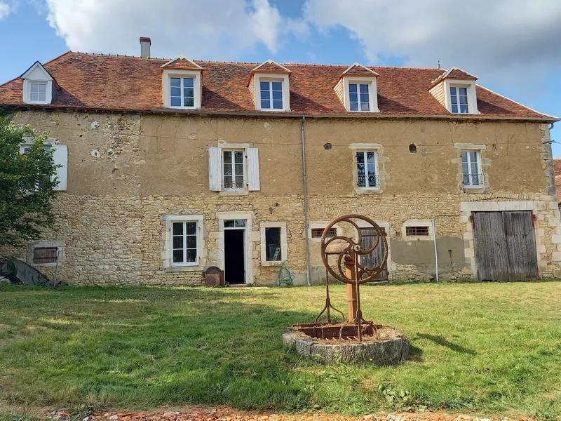 Façade en pierre du corps de logis avec quatre lucarnes sur toit de tuiles et grande pelouse