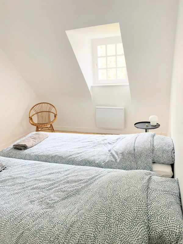 Chambre sous mansarde avec lit double, couette imprimée et fauteuil en rotin