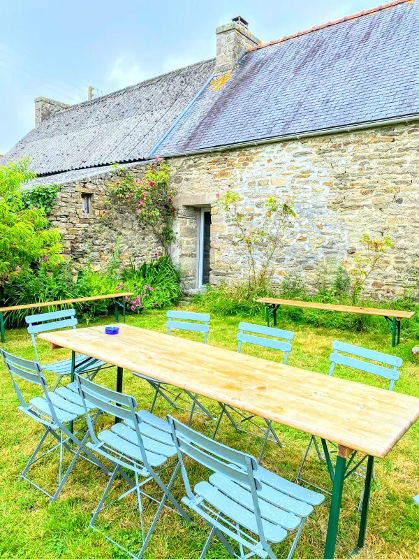 Espace repas extérieur avec longues tables en bois et chaises pliantes devant la façade en pierre