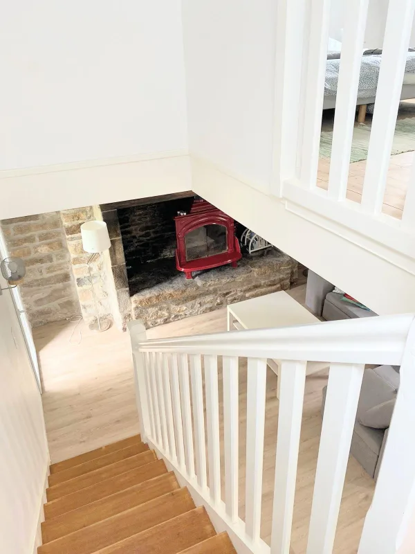 Vue plongeante depuis l'escalier vers le séjour avec poêle rouge dans cheminée en pierre