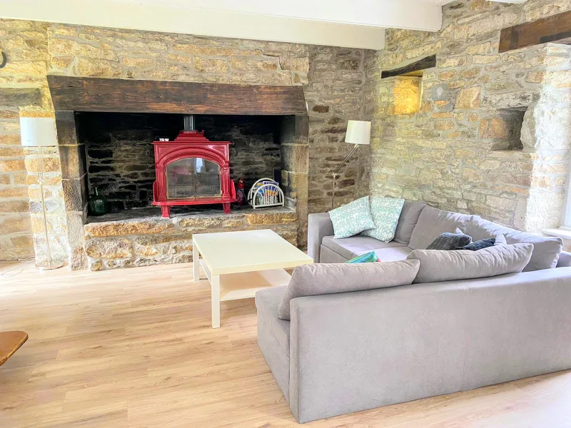 Séjour chaleureux avec murs en pierre apparente, poêle à bois rouge dans cheminée et canapé gris