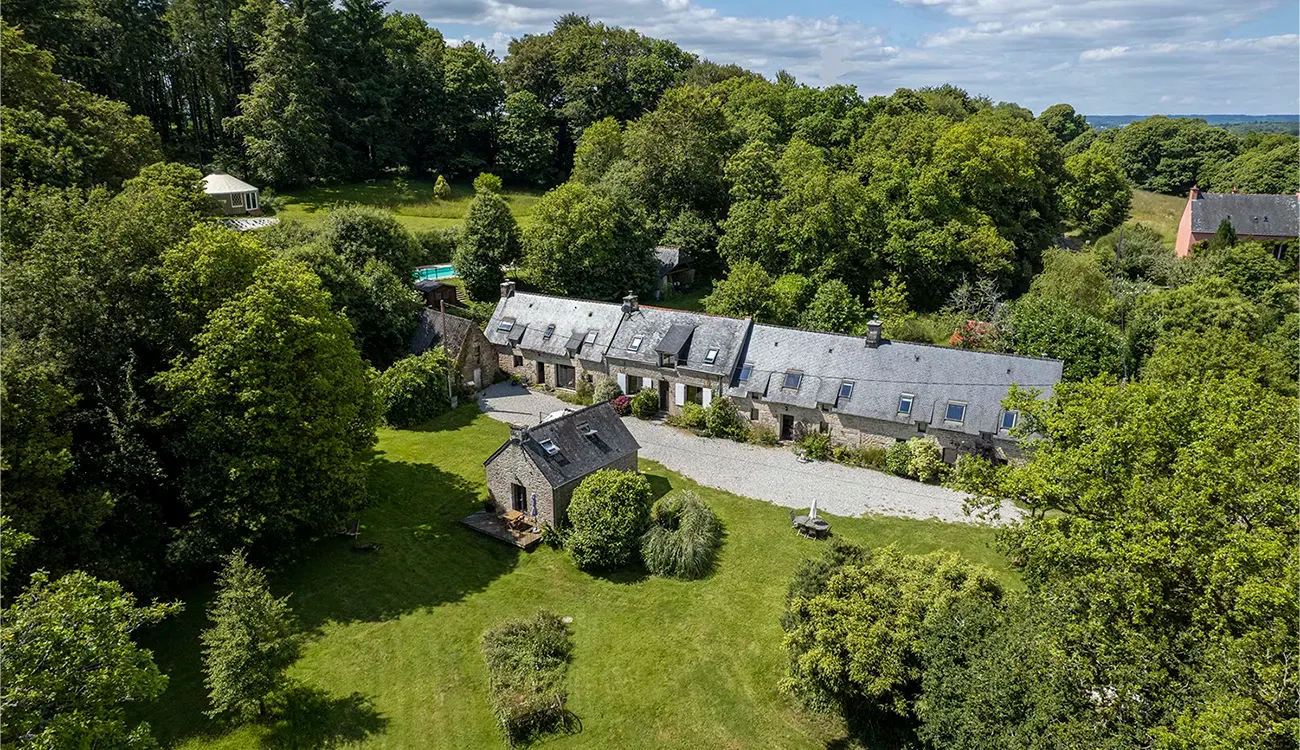 Gîte de groupe Forêt Totem à Persquen — Vue aérienne du domaine Forêt Totem avec ses longères en pierre, sa yourte et ses jardins au cœur de huit hectares de forêt, capacité 22 personnes