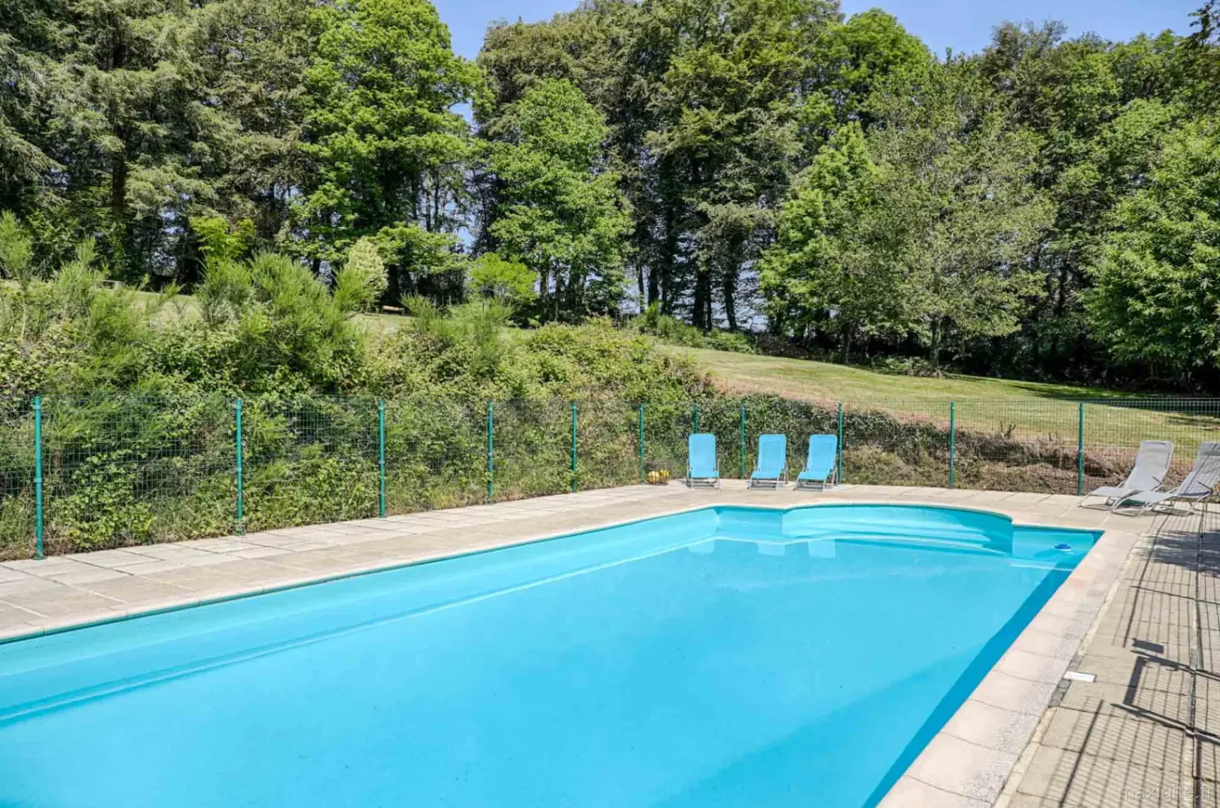 Piscine extérieure chauffée et sécurisée avec transats bleus, bordée d'arbres et de verdure