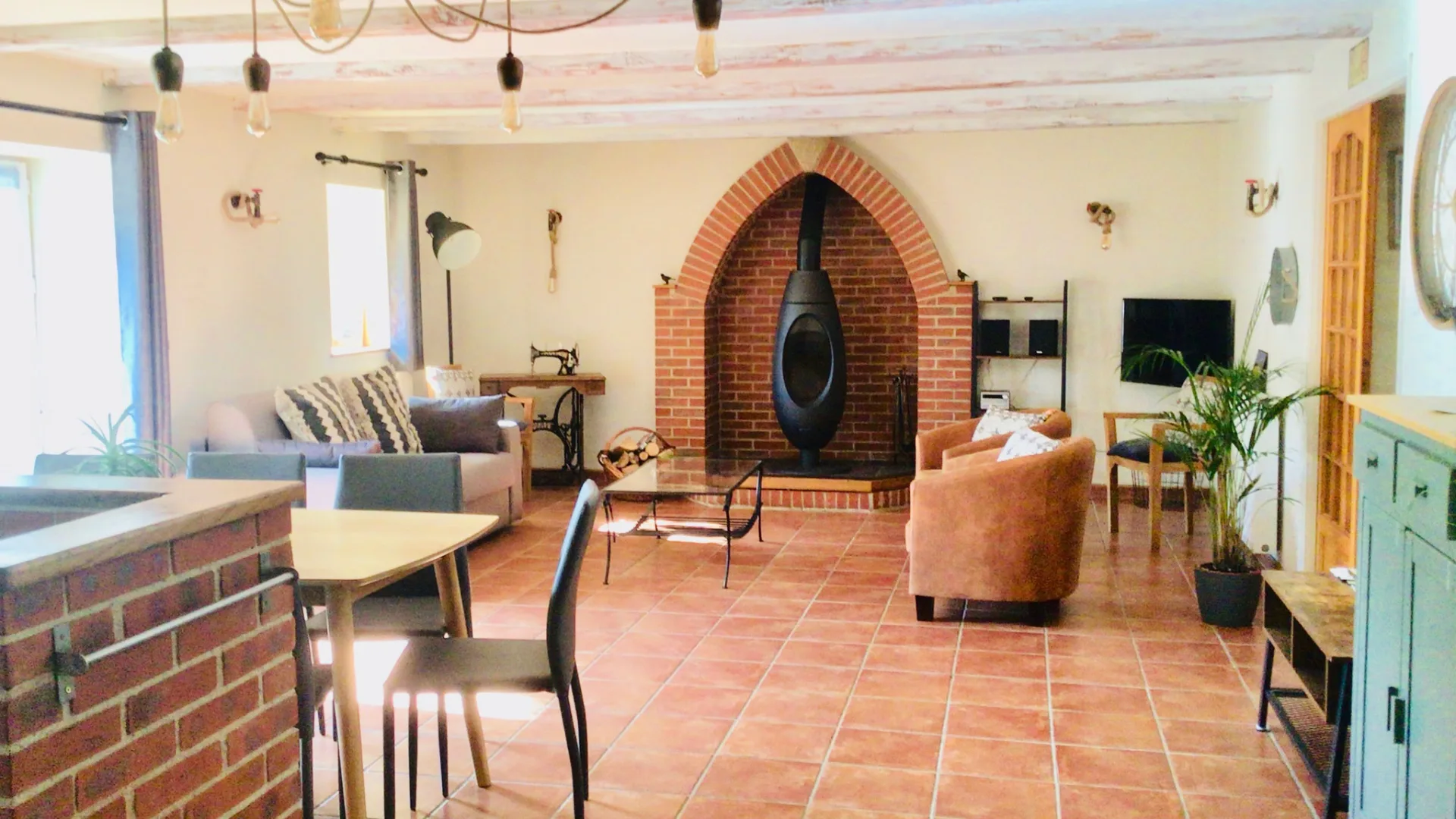 Grand séjour avec poêle à bois dans une arche en brique, canapés confortables et poutres blanchies