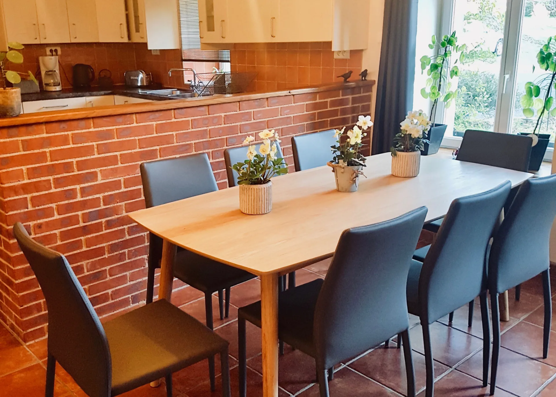 Salle à manger avec table dressée pour huit convives, cuisine ouverte et bar en brique