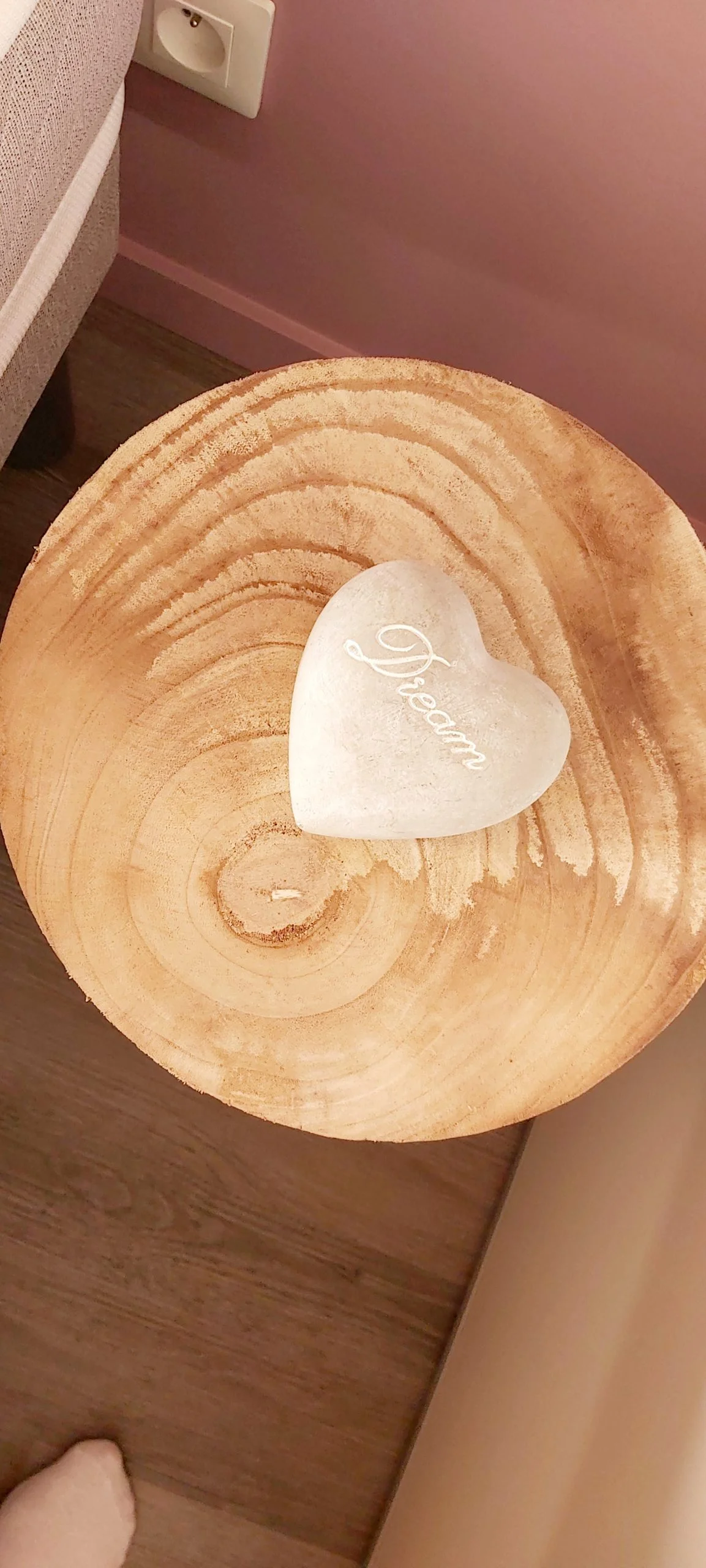 Table basse en tronc de bois avec objet décoratif en forme de cœur blanc gravé 'Dream', dans une chambre aux murs roses