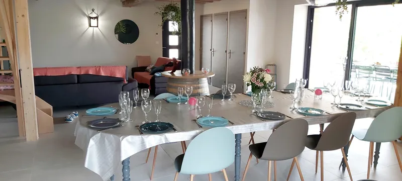 Grande salle à vivre lumineuse avec coin salon et poutres apparentes dans le gîte de groupe