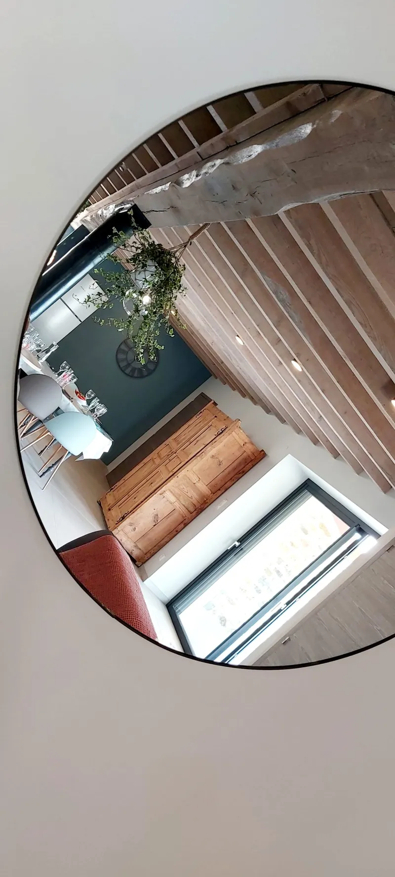 Miroir mural rond reflétant la charpente en bois, le buffet ancien et le coin repas de la salle à vivre