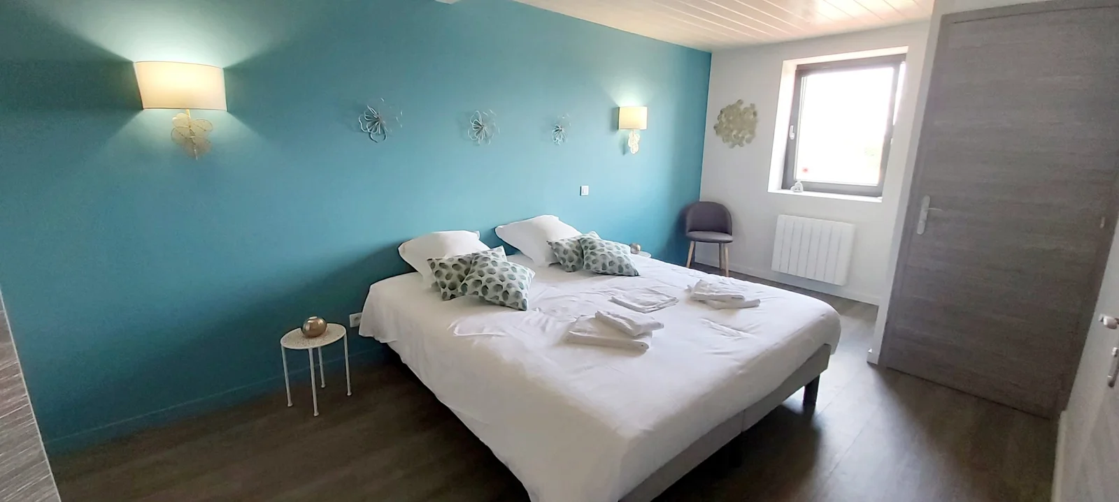 Chambre aux murs bleu turquoise avec lit double, appliques murales et petites fleurs décoratives en métal