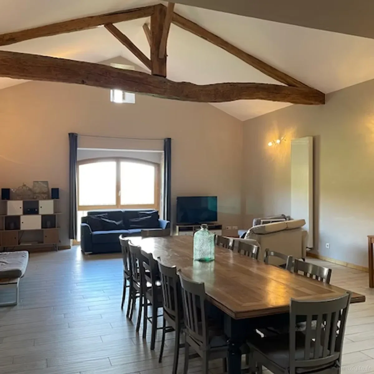 Séjour sous charpente en bois avec canapé bleu marine, télévision et grande table à manger en arrière-plan