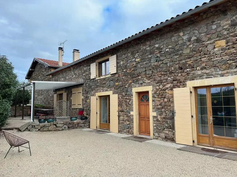 Façade en pierres dorées du gîte avec volets beiges et portes en bois donnant sur la cour