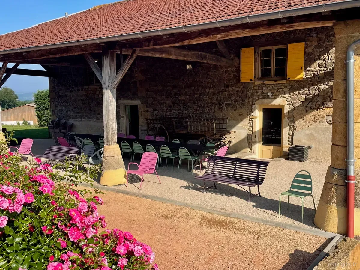 Terrasse couverte du domaine avec bancs et chaises roses et vertes sous un auvent en tuiles rouges