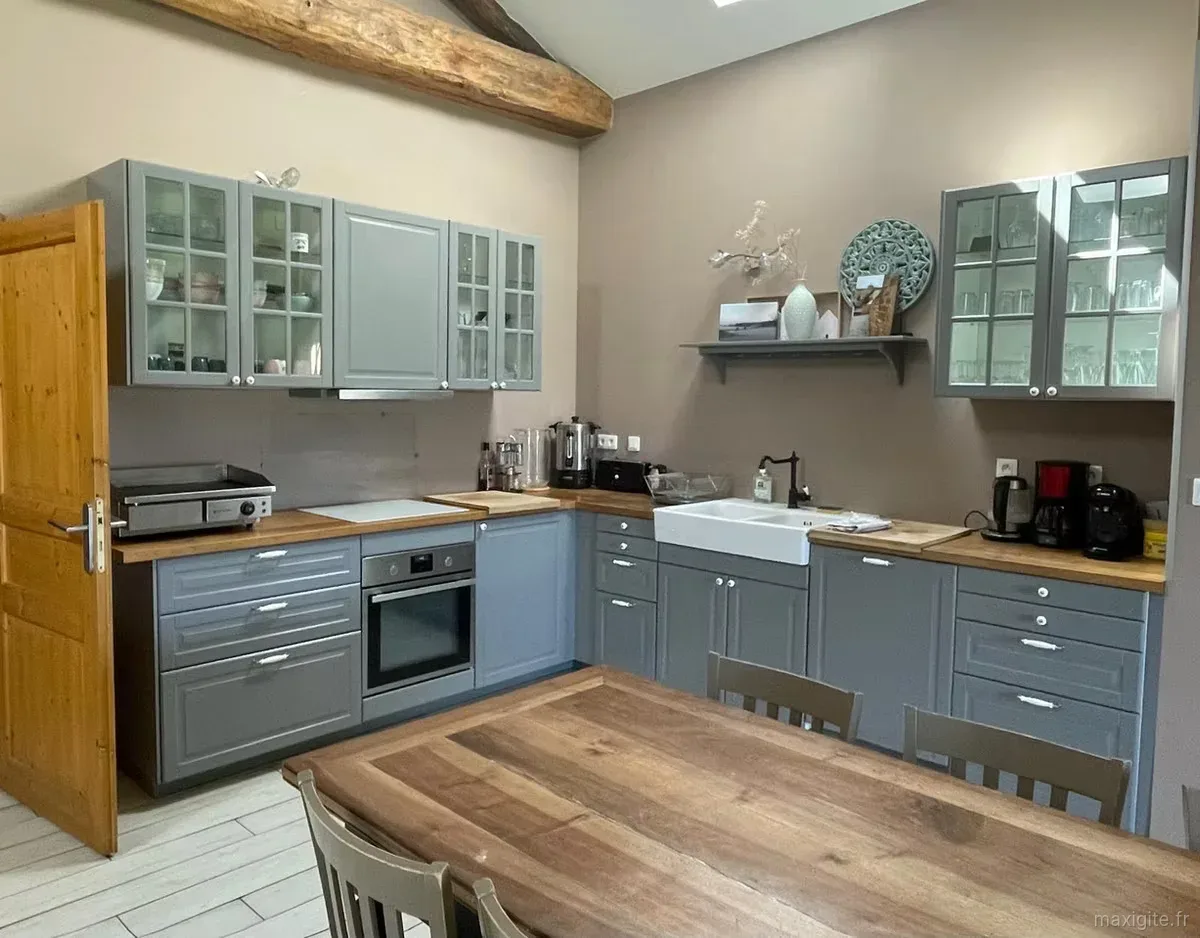 Cuisine équipée avec meubles gris, plan de travail en bois et évier double sous une poutre apparente