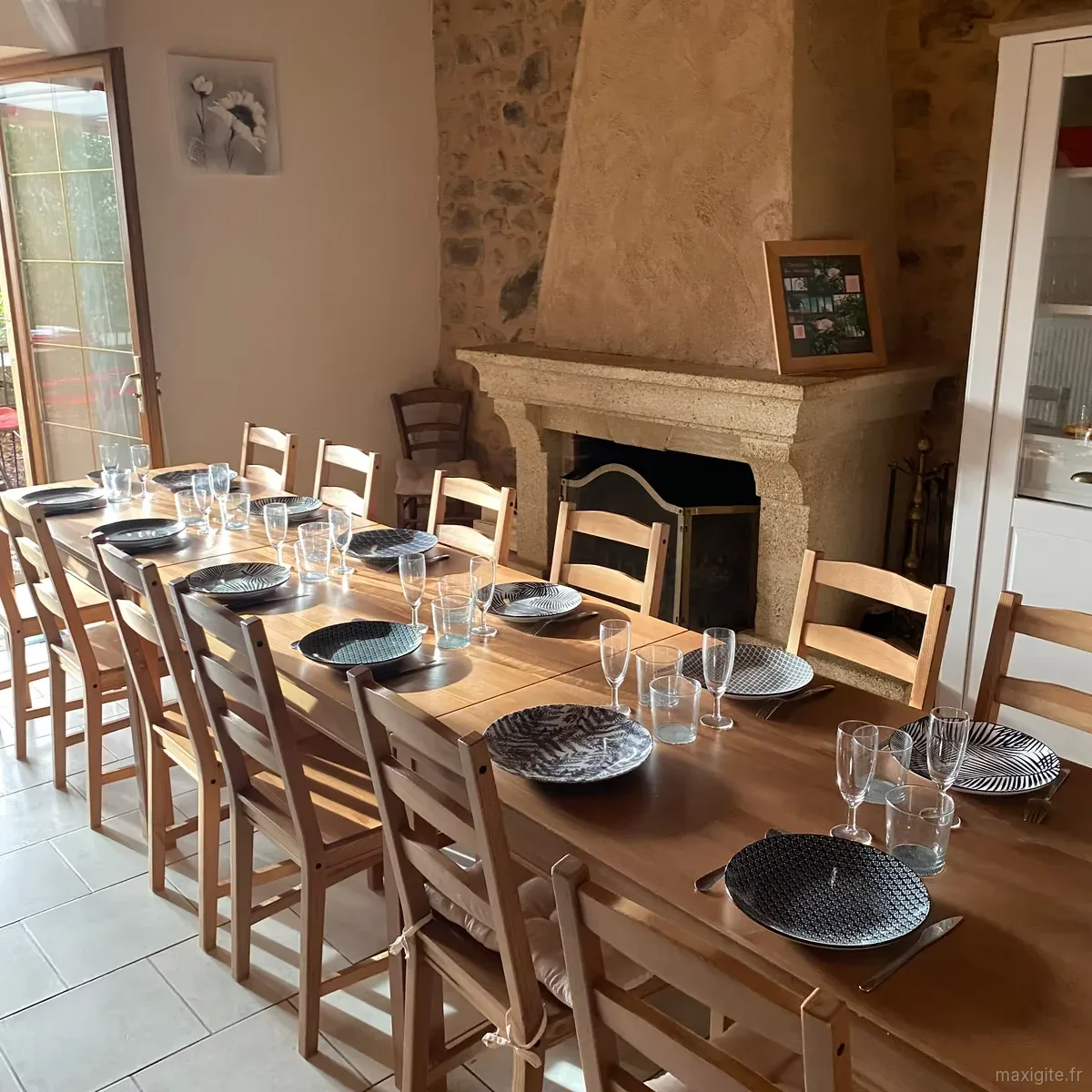 Salle à manger voûtée en pierre avec cheminée ancienne et longue table dressée d'assiettes à motifs noir et blanc