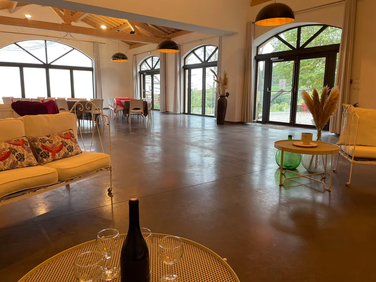 Grande salle de réception à charpente bois avec portes vitrées ouvertes sur le jardin et tables dressées