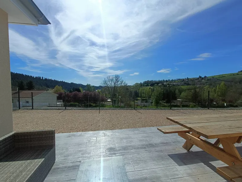 Vue panoramique depuis la terrasse du gite sur la campagne du Haut-Beaujolais avec collines boisees et ciel bleu
