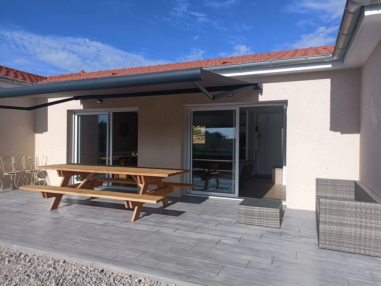 Gîte de groupe Gite l'Ambremy à Cublize — Terrasse du gite l'Ambremy avec table de pique-nique en bois, store banne deploye et baies vitrees ouvrant sur la piece de vie, capacité 11 personnes