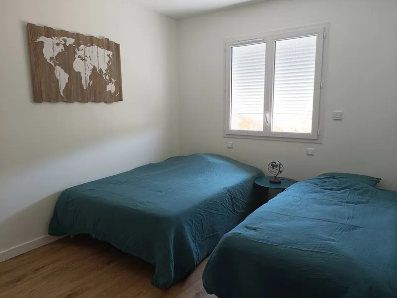 Chambre twin avec deux lits simples, literie bleue et decoration murale carte du monde