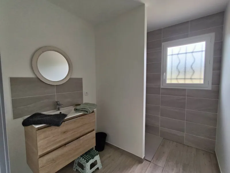 Salle d'eau avec douche a l'italienne, miroir rond et meuble vasque en bois