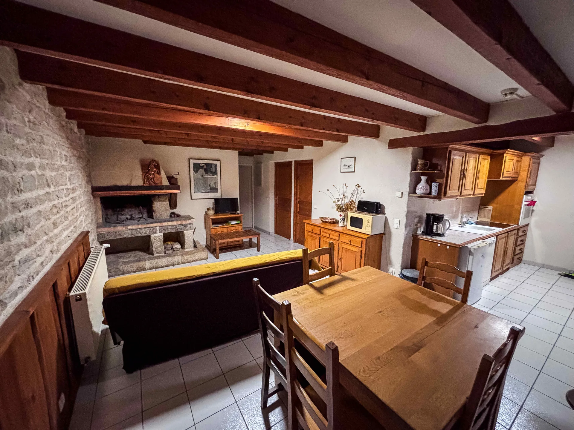 Séjour de l'Appart avec mur en pierre, poutres apparentes, buffet ancien et canapé sombre à coussin moutarde