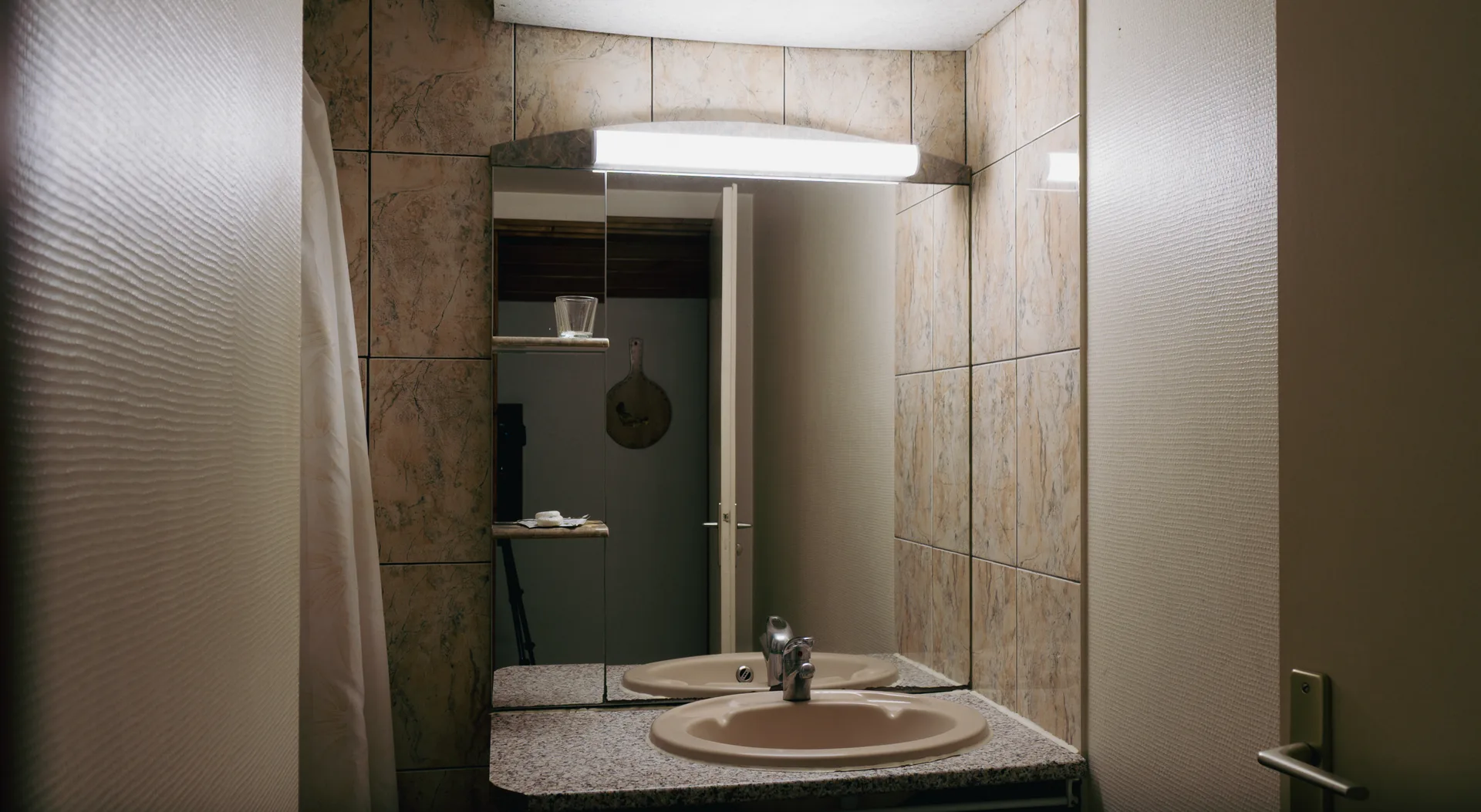 Salle de bain aux murs carrelés effet granit, vasque ovale et miroir éclairé
