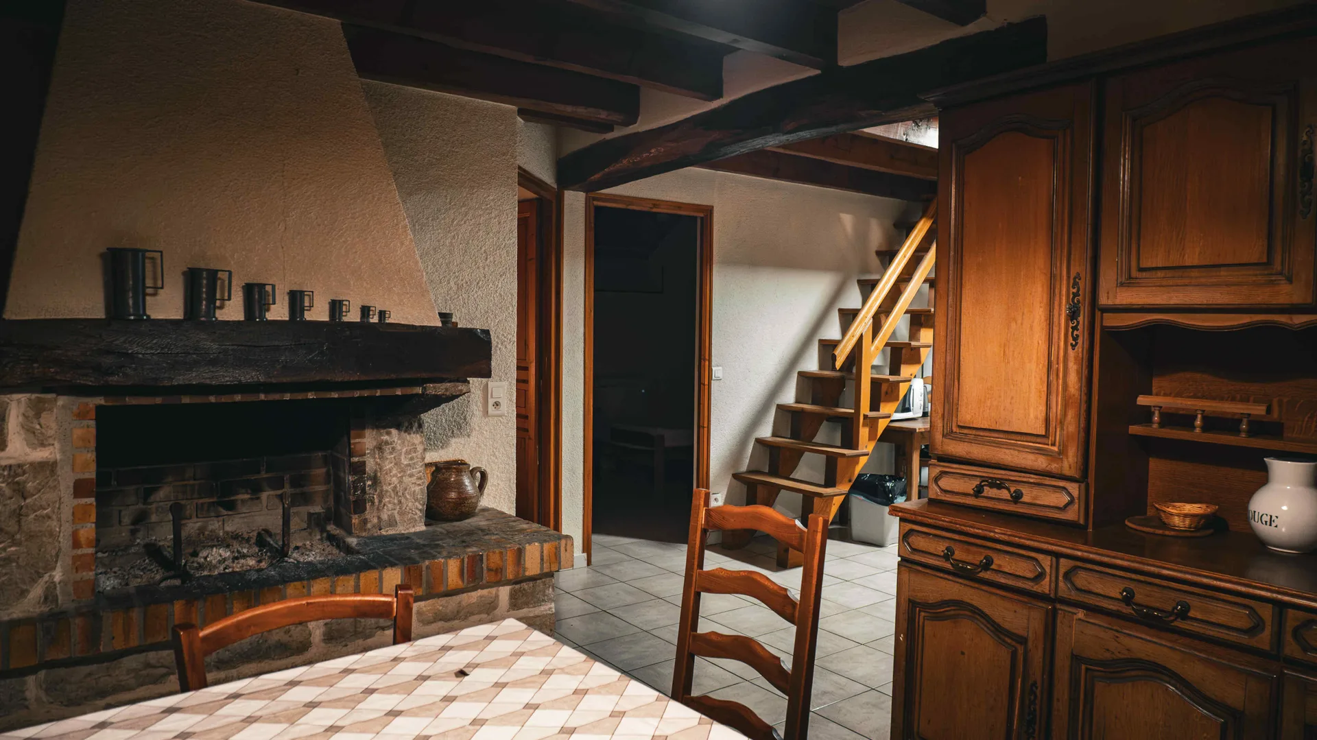 Cheminée en pierre garnie de chopes en étain, escalier en bois et buffet ancien avec pichet blanc
