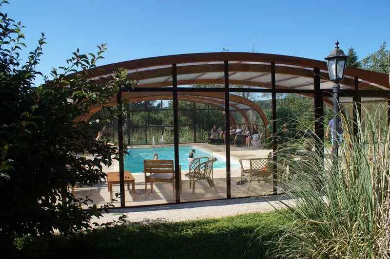 Piscine couverte sous verrière en bois arrondie, entourée de verdure