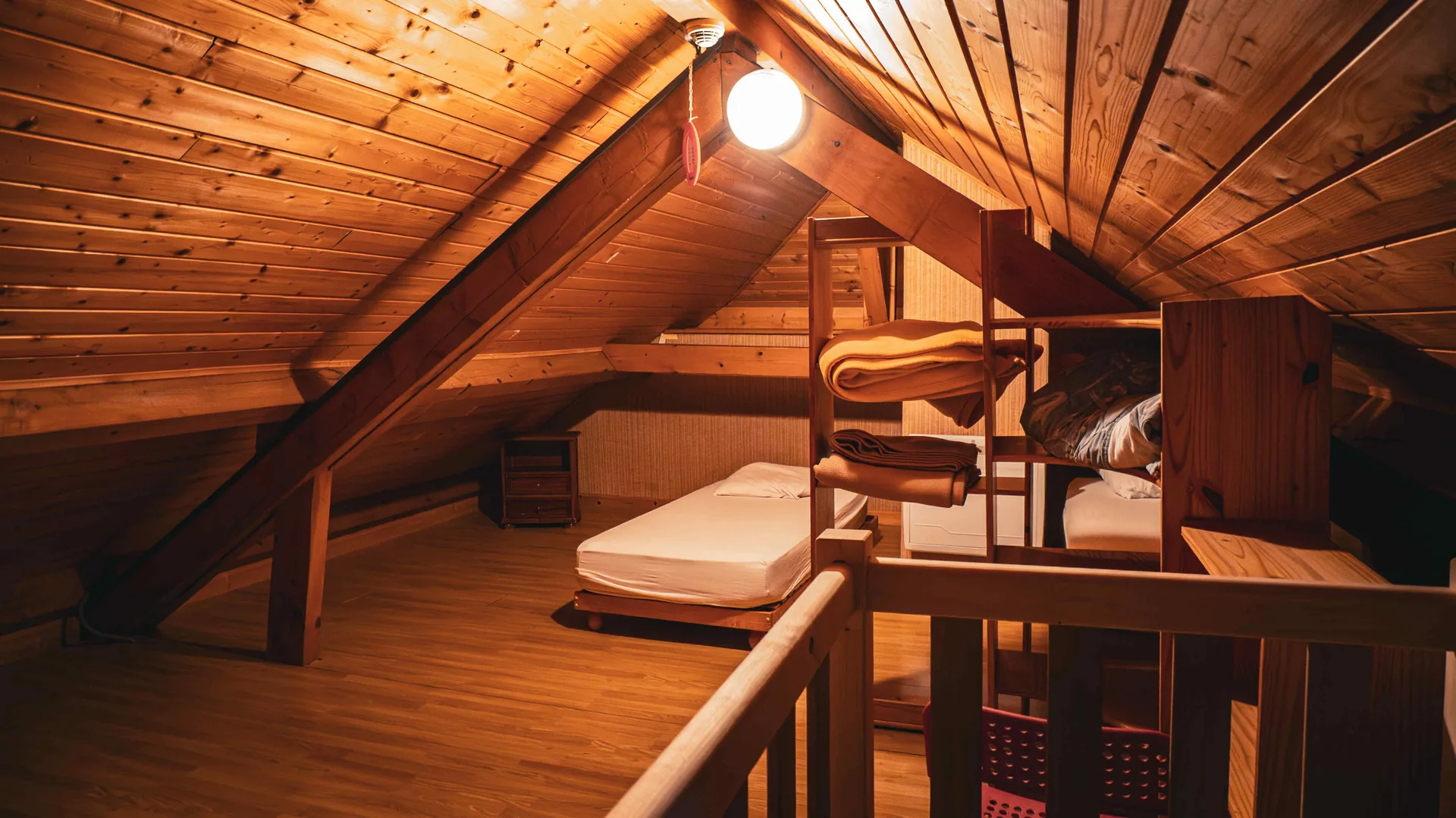 Chambre mansardée sous toit en bois en pente, deux lits simples et couvertures pliées sur échelle porte-linge