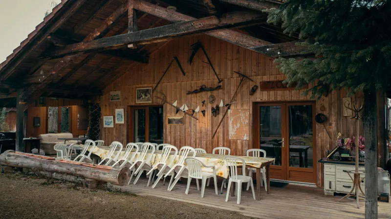 Façade en bois du gîte avec longue table dressée de nappes à motif tournesol et outils agricoles anciens accrochés au mur