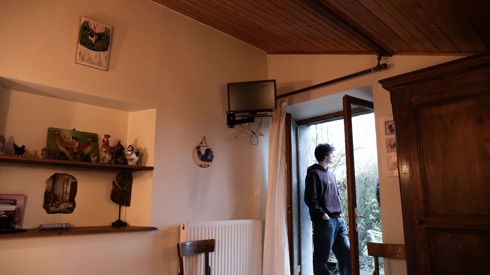 Pièce à vivre avec télévision murale et porte ouverte sur le jardin, petits objets décoratifs en forme de coq