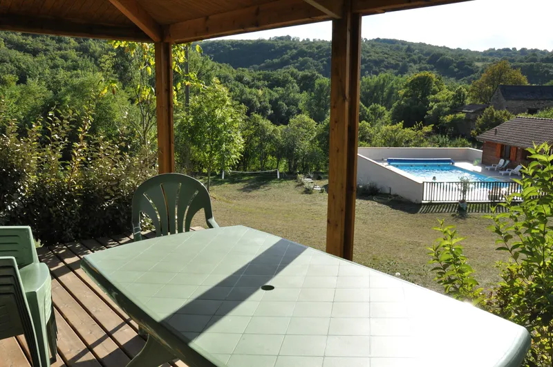 Terrasse couverte avec table et chaises vertes, vue dégagée sur la piscine et les collines boisées