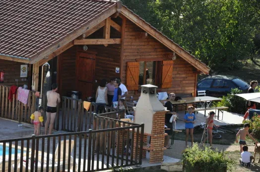 Vue en hauteur d'un chalet avec cheminée barbecue en brique, baigneurs en maillot et voiture garée à proximité