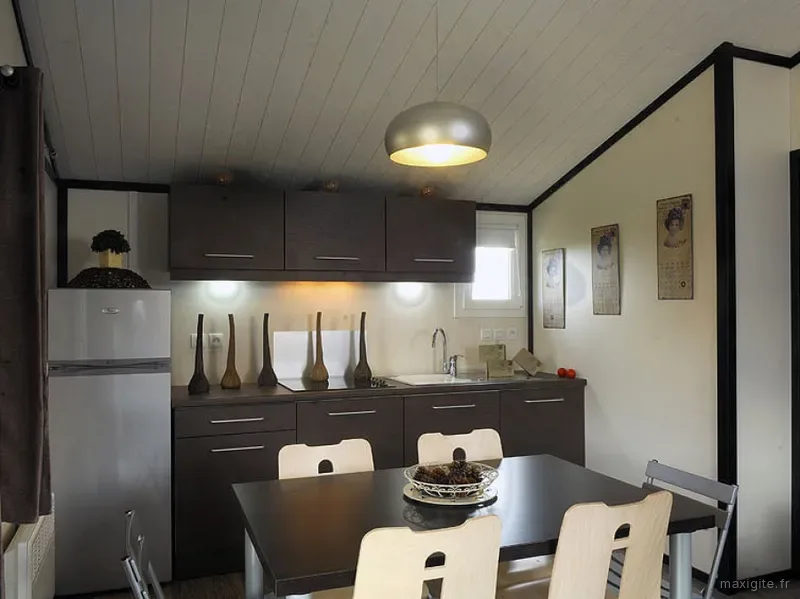 Coin cuisine-repas d'un chalet avec meubles gris foncé, réfrigérateur et affiches vintage encadrées au mur