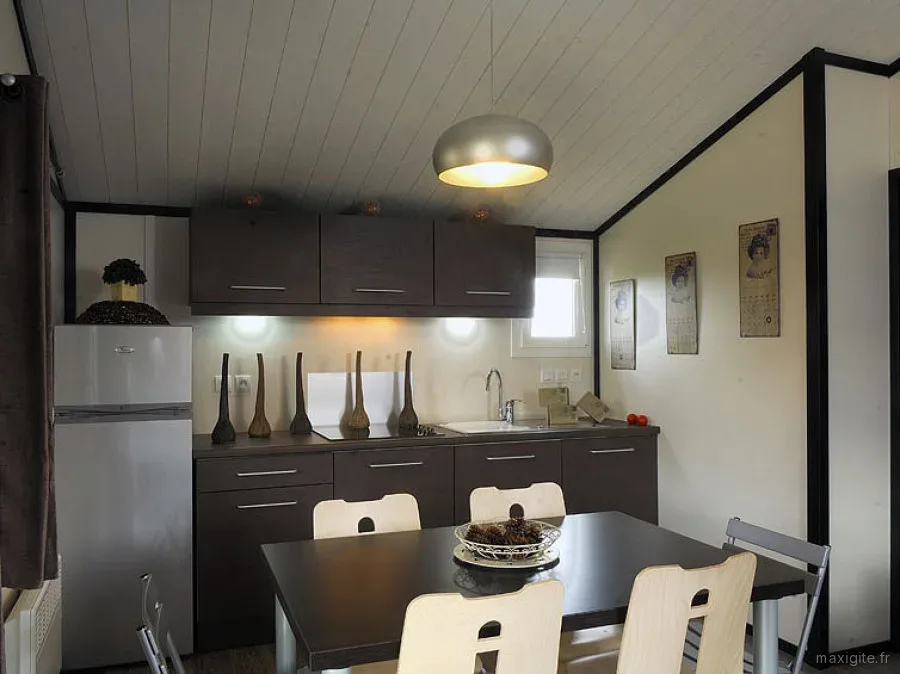 Coin cuisine-repas d'un chalet avec meubles gris foncé, réfrigérateur et affiches vintage encadrées au mur
