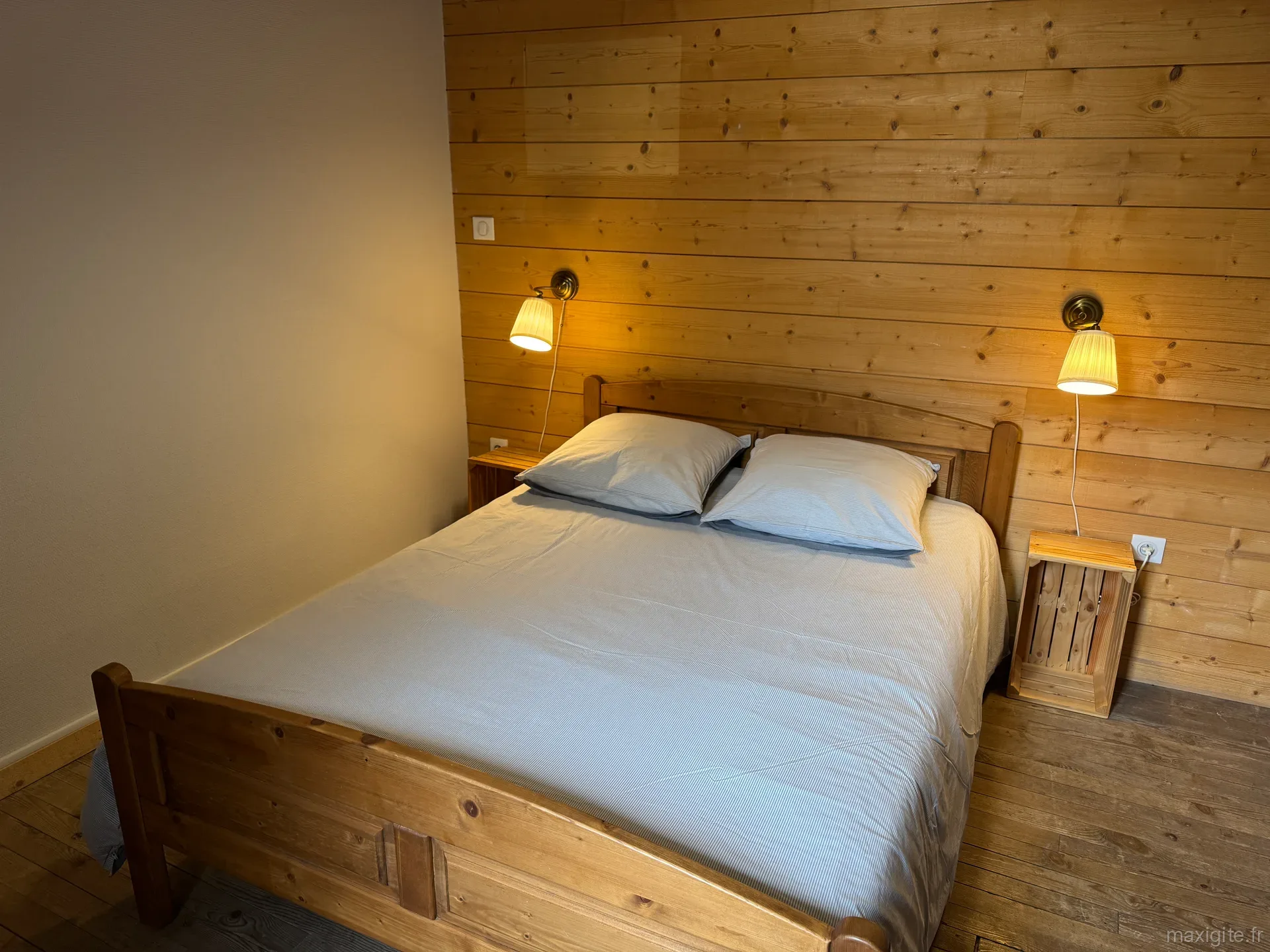 Chambre double aux murs lambrissés de bois clair, lit en bois et chevet fabriqué à partir d'une caisse