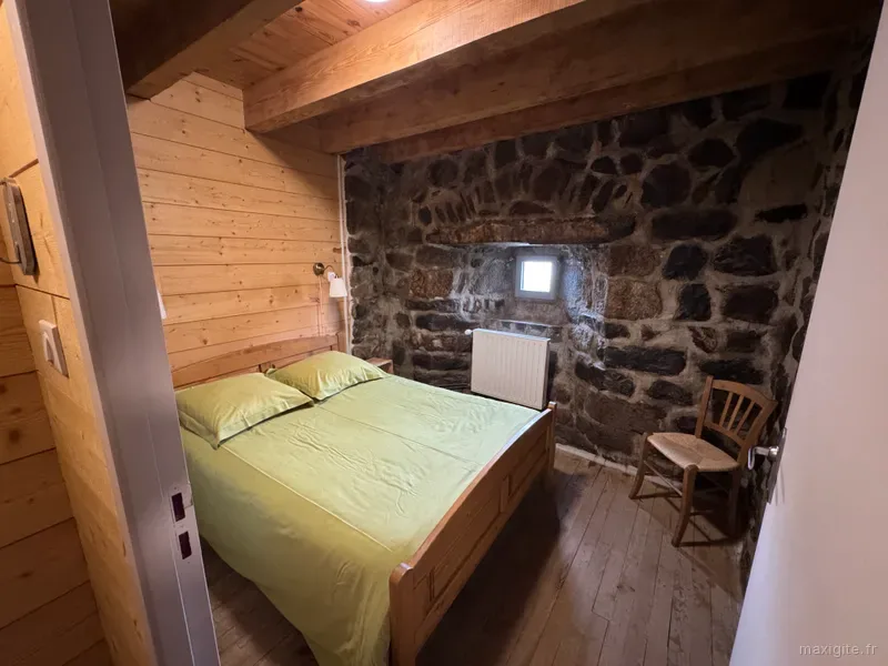 Chambre avec alcôve en pierre apparente, literie vert anis et chaise paillée en bois