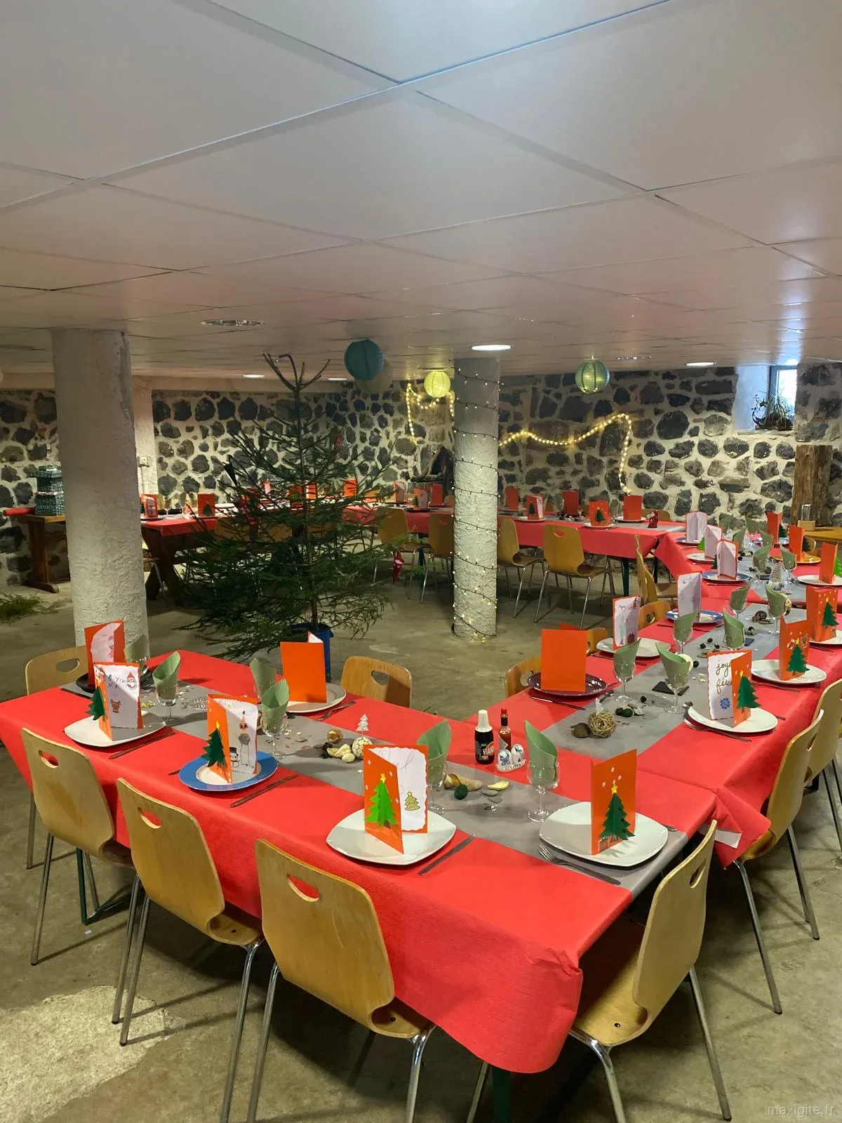Grande salle de réception voûtée en pierre, tables dressées de nappes rouges et sapin de Noël décoré