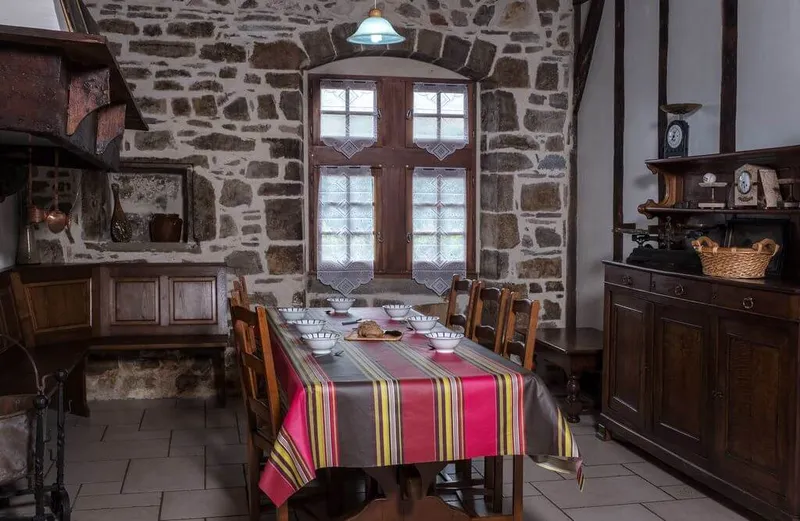 Coin repas voûté en pierre avec fenêtre à rideaux brodés, buffet ancien et balance de cuisine ancienne