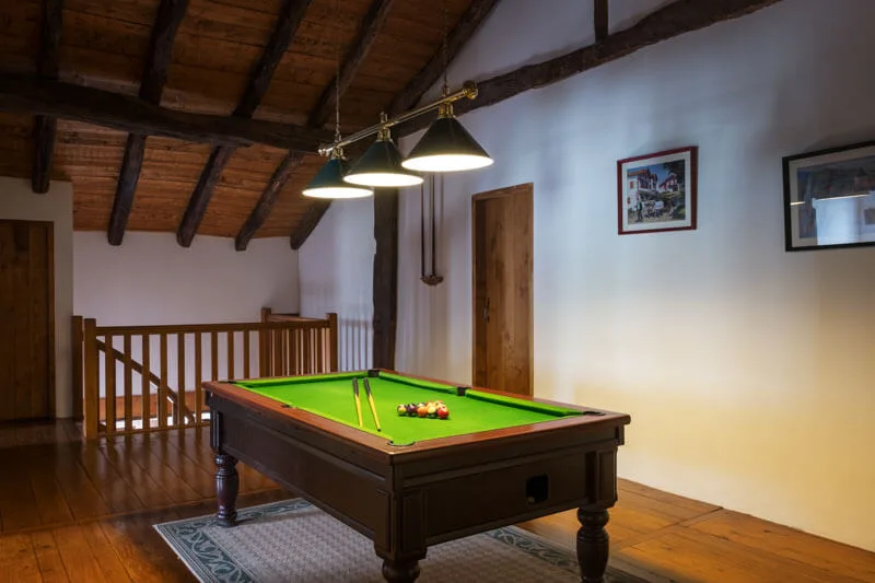Billard sous charpente en bois avec boules disposées en triangle et escalier menant à l'étage inférieur