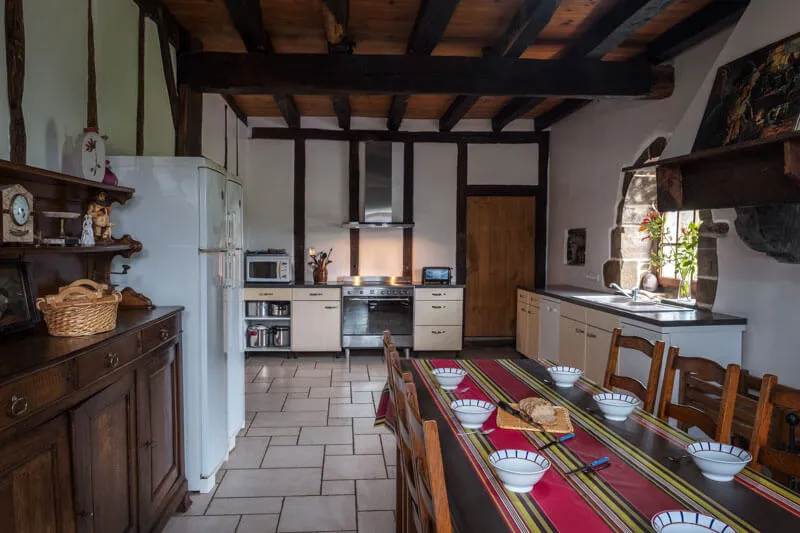Cuisine sous poutres apparentes avec réfrigérateur blanc, hotte inox et table dressée de bols et de pain