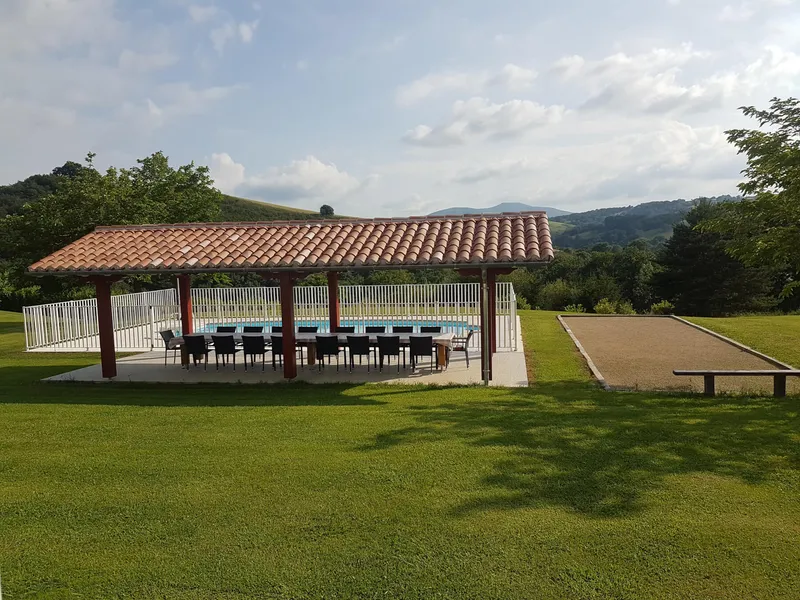 Pavillon couvert à toit de tuiles rouges avec longue table pour une quinzaine de convives, boulodrome et vue sur les collines