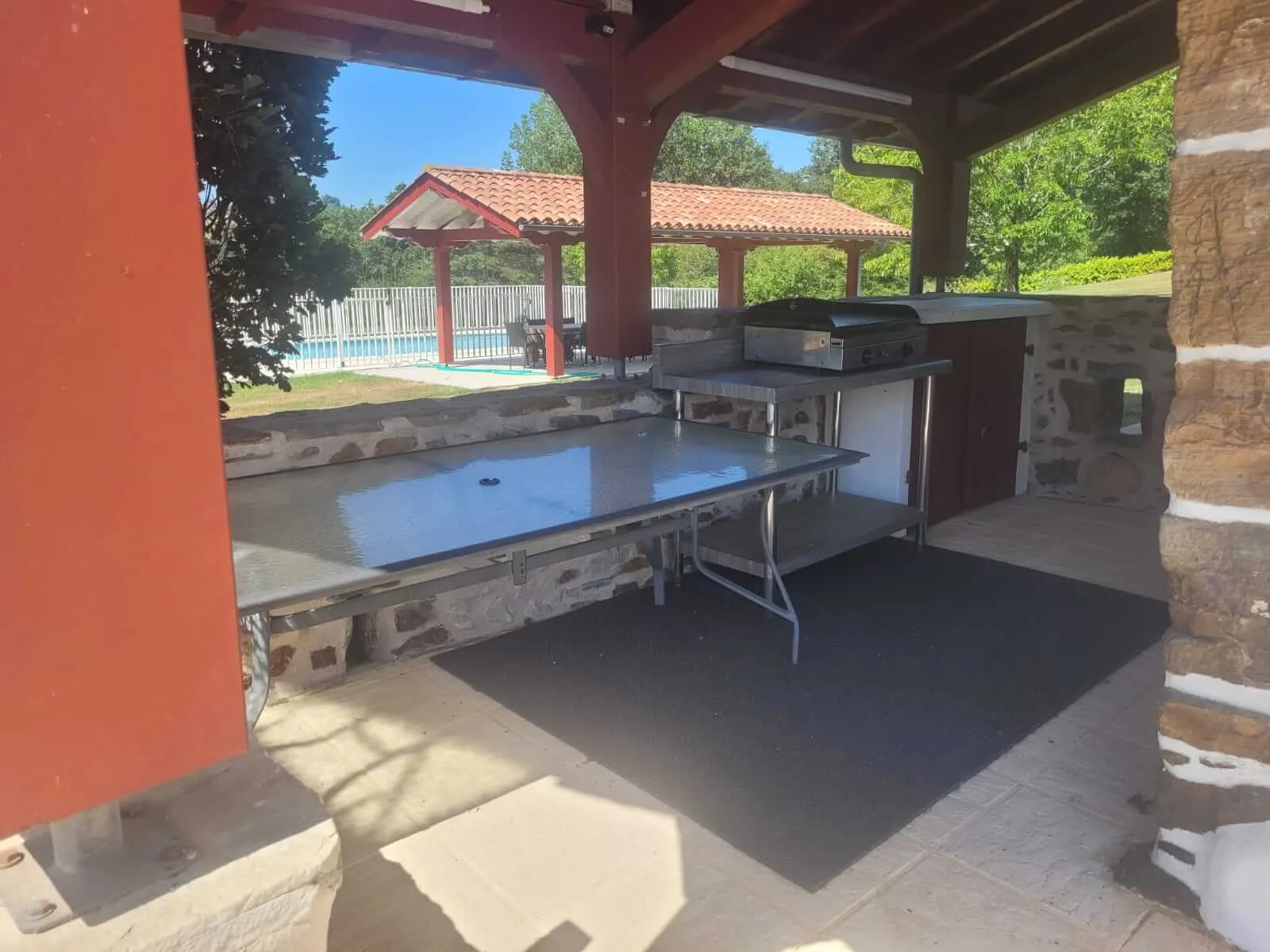 Coin plancha extérieur couvert avec plaque de cuisson inox et grande table en inox, vue sur la piscine