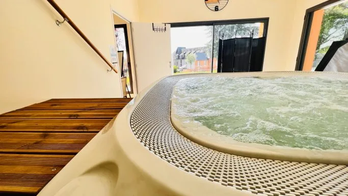 Bain à remous intérieur en carrelage clair avec terrasse en bois attenante et baies vitrées sur le jardin